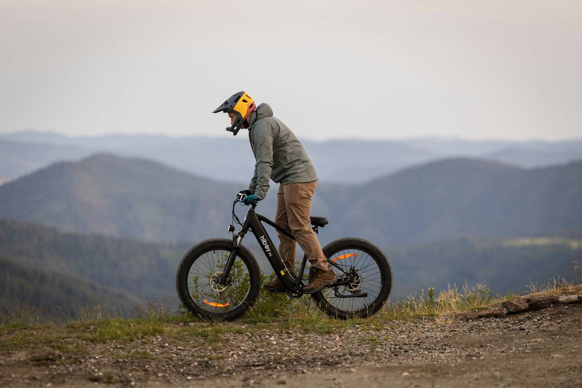 Rider on hill ebike adventure navigating a pine-forested mountain trail with snow-capped peaks in background